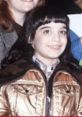 Young girl with dark hair and a golden jacket, smiling, representing Danielle Brisebois during her early career.