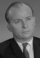 William Woodson with a serious expression, wearing a suit and tie, set against a neutral backdrop. Classic black and white style.