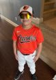 Young baseball player in Orioles gear smiling confidently, ready for practice or a game in vibrant orange and white uniform.