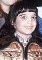 Young girl with dark hair and bangs, wearing a brown coat, smiling in a nostalgic setting related to Danielle Brisebois.