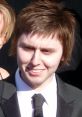 Jay Cartwright, portrayed by James Buckley, smiles in a tuxedo, showcasing a youthful appearance and stylish look.