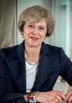 Theresa May smiling in a formal setting, dressed in a dark suit with pearl necklace, showcasing her leadership presence.