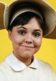 Sally Field smiles warmly in a vintage costume against a bright yellow background, showcasing her iconic youthful charm.