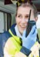 Smiling woman in safety gear using a two-way radio, actively engaged in communication during a field operation.