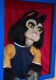 Crusty the Cat puppet with striking features, wearing a blue shirt, displayed in a vibrant blue and red setting.