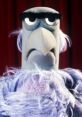 Sam the Eagle, created by Frank Oz, displays a stern expression against a red curtain backdrop.