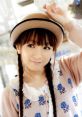 Yui Horie smiling playfully, wearing a stylish hat and a cute, patterned sweater in a light-filled environment.