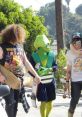 Wavves band members and an alien figure walk together with skateboards in a vibrant outdoor setting from "Way Too Much.