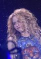 Shakira performing energetically, showcasing her signature curly hair and vibrant outfit during a concert for 'Loba.