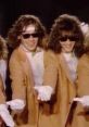 Van Halen's "Hot For Teacher" video features energetic performers in sunglasses and beige coats, capturing the playful spirit.