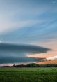 Dramatic supercell clouds over a lush green field at sunset, showcasing nature's powerful meteorological phenomena.