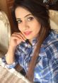 Miss Pooja casually poses with a charming smile, showcasing her stylish plaid shirt and long, flowing hair.