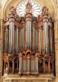 Ornate church organ with grand pipes and intricate woodwork, set against a stunning stained glass window backdrop.