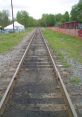 View down a rustic railway track surrounded by greenery and a tent, showcasing the charm of rural train routes.