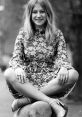 Young woman in a floral dress sitting on a rock, exuding a cheerful vibe with a relaxed pose and long hair.