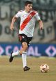 Fernando Fernandez dribbles the ball on the field wearing River Plate's iconic white and red jersey during a match.