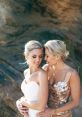 Two brides embrace, radiating love and joy in a beautiful outdoor wedding setting, celebrating their special day together.