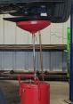 Red oil catch can positioned under a vehicle, showcasing automotive maintenance equipment in a workshop setting.