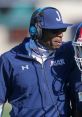 Coach discussing strategy in a Big Twelve Conference football game, wearing headphones and team apparel.