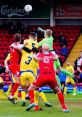 Kidderminster Harriers players compete for a high ball during an intense football match at Aggborough Stadium.