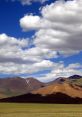 Majestic Mongolian mountains under a bright blue sky with fluffy white clouds, showcasing nature's serene beauty.