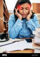 Stressed woman holding her head in a library, surrounded by books and notes, reflecting the pressures of academic life.