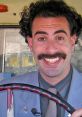 Borat character smiling widely while driving, showcasing humor and unique style in a playful, comedic setting.