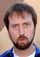 Tom Green with a distinctive expression, wearing a blue shirt, showcasing his unique comedic style and personality.