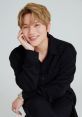 Kwill smiles warmly, dressed in a stylish black shirt, showcasing a charming and playful personality.