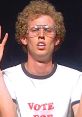 Napoleon Dynamite character with curly hair wearing a "Vote for Pedro" shirt, looking determined during a school presentation.