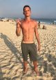 Young man with a confident pose on a sunny beach, wearing green shorts and showing a playful gesture, capturing summer vibes.