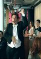 Dancing waiter in a tuxedo entertains patrons in a lively cafe setting, featuring a fun atmosphere for the Go Compare advert.