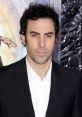 Actor at a premiere event, known for the character Borat, showcasing a suave look in a black suit and white shirt.