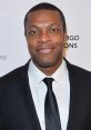 Chris Tucker smiles confidently in a formal suit, showcasing his charismatic personality and style at a public event.