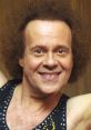 Smiling Richard Simmons with curly hair, wearing a colorful tank top, radiating energy and positivity in a lively fitness setting.