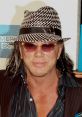 Mickey Rourke at a premiere event, wearing a stylish fedora and sunglasses, showcasing his unique fashion sense.