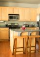 Modern kitchen featuring light wooden cabinets, stainless steel appliances, and a central island with bar stools.