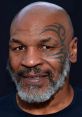 Mike Tyson with a distinct facial tattoo and greying beard, smiling against a dark background, showcasing his iconic look.