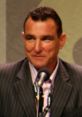 Vinnie Jones at a speaking event, sporting a suit, microphone in hand, showcasing his charismatic personality.