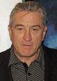 Robert De Niro with a serious expression, wearing a black blazer and striped shirt, showcases his iconic look in film.