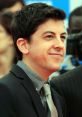 Actor portraying McLovin from Superbad smiles at a red carpet event, dressed sharply in a suit and tie.