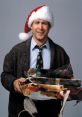 Clark W. Griswold, wearing a Santa hat, smiles while holding messy gift-wrapped presents, embodying holiday cheer.