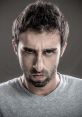 Angry young man with intense expression, showcasing annoyance and frustration in a gray shirt against a neutral background.