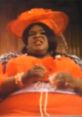 Fluisa from Deuce Bigalow in vibrant orange attire, showcasing bold fashion and memorable character in a comedic scene.