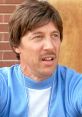 Kip from Napoleon Dynamite with a surprised expression, wearing a light blue sweater, against a brick background.