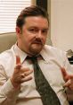 David Brent gestures playfully in an office setting, embodying humor from the "Prank Call" scene.