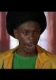 Dave Chappelle's iconic prank call character, wearing a bright yellow jacket and reacting humorously during a scene.