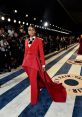 Janelle Monáe stuns in a bold red suit with dramatic cape, walking the Vanity Fair Oscars red carpet.