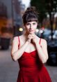 Young woman in a red dress poses thoughtfully outdoors in an urban setting, capturing a moment of elegance and charm.