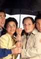 Jerry Seinfeld and friends sharing a light-hearted moment under an umbrella, showcasing friendship and humor from the iconic sitcom.